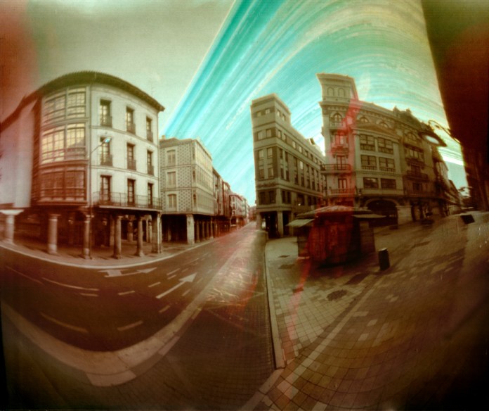 Fotografías de una ciudad en paletas grises y pastel y un trazo de color en el cielo hecho por el paso del sol por el cielo sobre la película fotosensible.