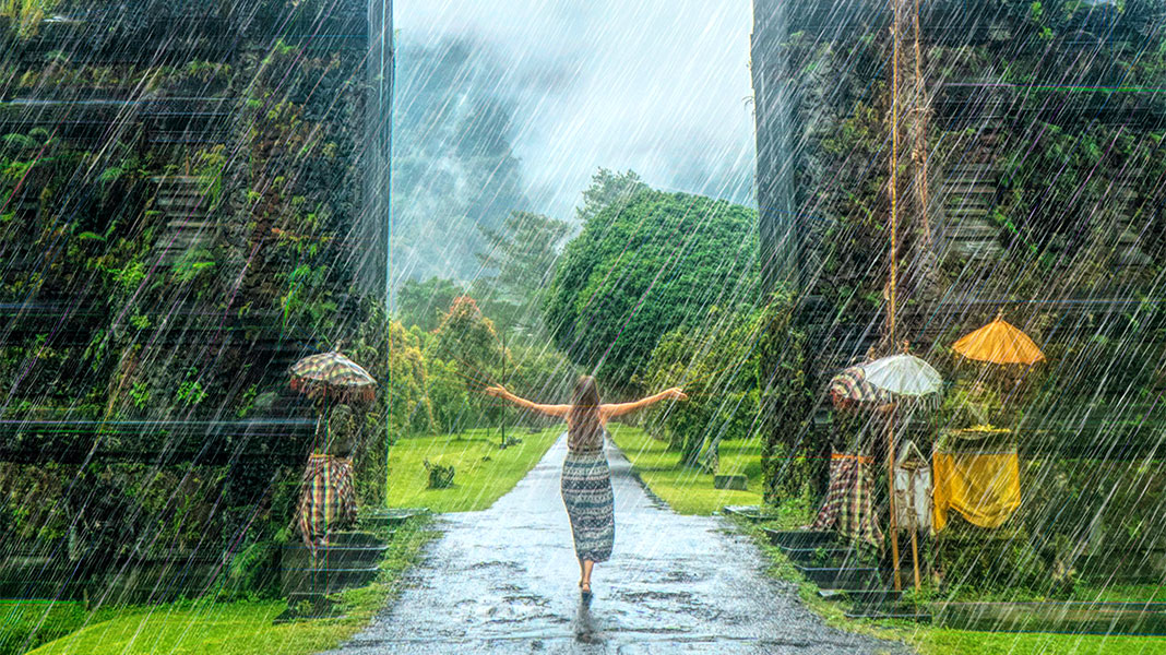 Mujer entrando en monumento natural en Bali mientras caen chuzos de punta.