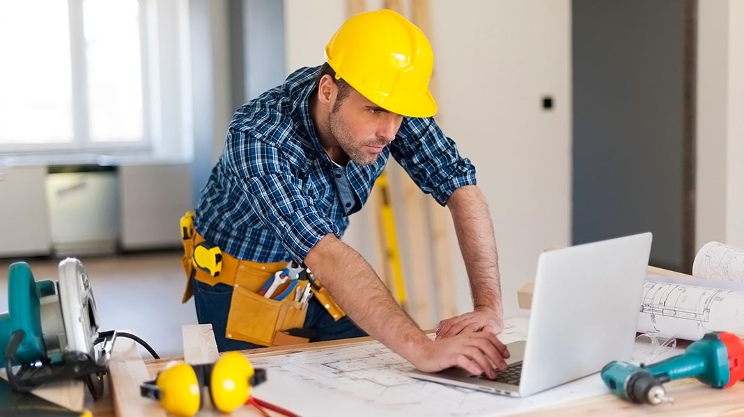 Constructor con casco de protección mirando un ordenador portátil