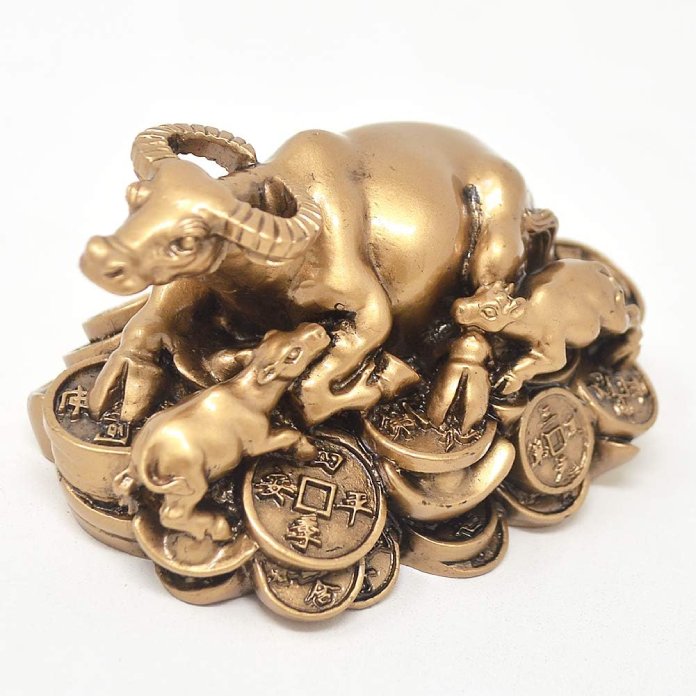 Estatuilla dorada de un buey con dos crías y monedas chinas.