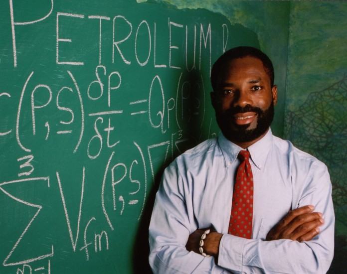 Philip Emeagwali posando al lado de una pizarra con ecuaciones diferenciales garabateadas.