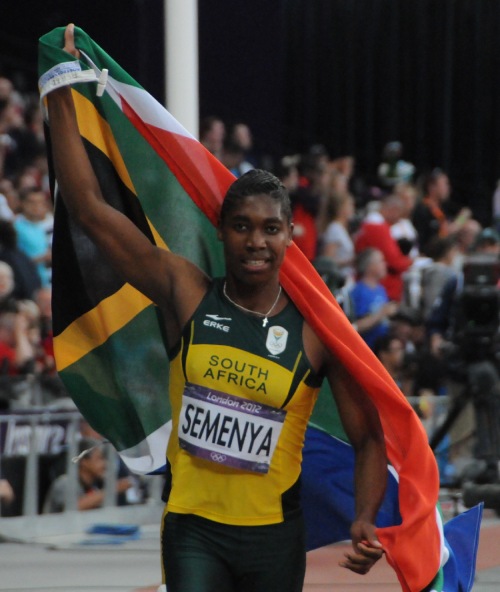 Caster Semenya, corredora, atleta profesional corriendo con la bandera de su país.