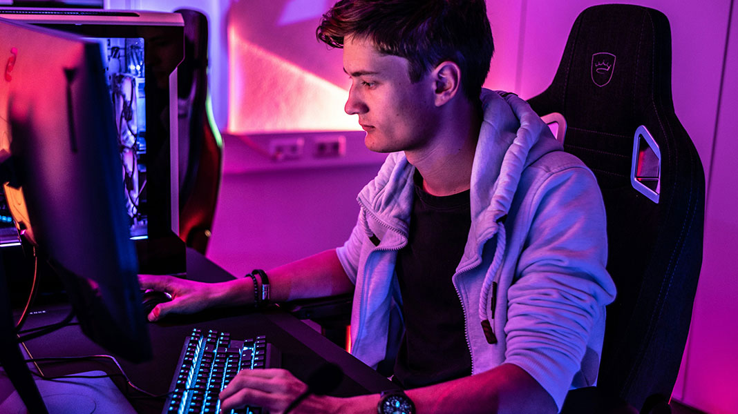 Gamer jugando a videjuegos en una habitación iluminada en rosa, con ordenador y silla de gamer