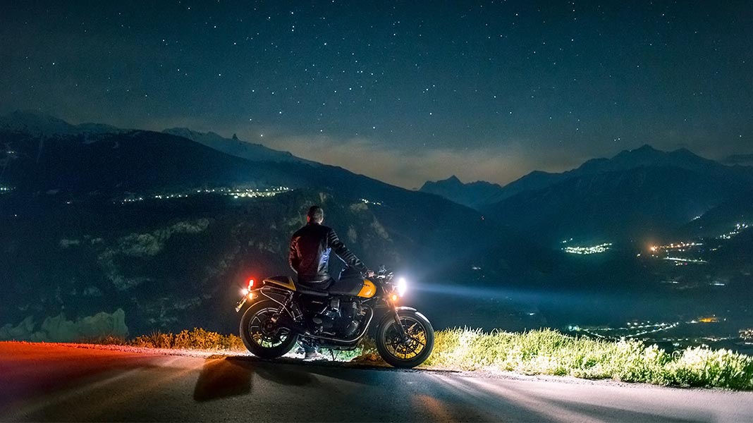 motorista parado de noche en un mirador junto a su moto